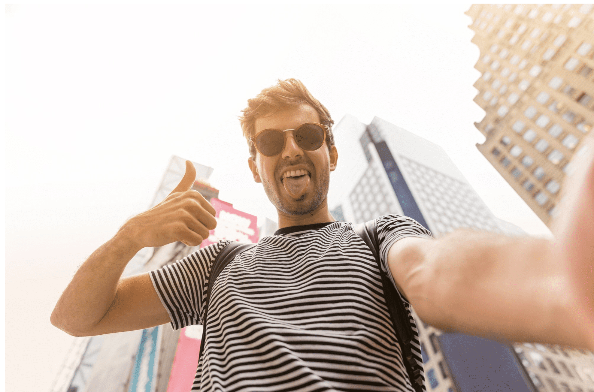 Man taking a selfie with his phone in a bustling city street, smiling and enjoying the moment.