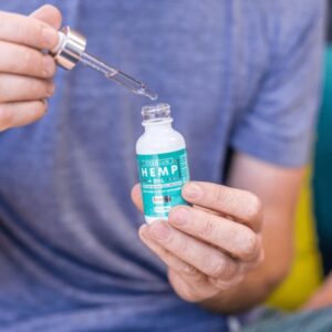 A bottle of Pure Standard Extracts CBD Delta-8 + CBD oil tincture with its packaging displayed on driftwood, featuring product information and supplement facts, outdoors with greenery in the background.