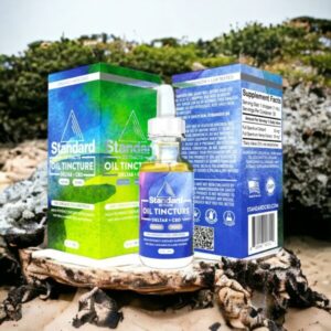 Three boxes and a bottle of Standard Extracts Oil Tincture (Delta 8 + CBD) rest on sandy ground outdoors with greenery in the background, inviting questions like how long does Delta-8 stay in your system
