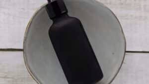 An unlabeled black dropper bottle resting in a grey ceramic bowl on white wood