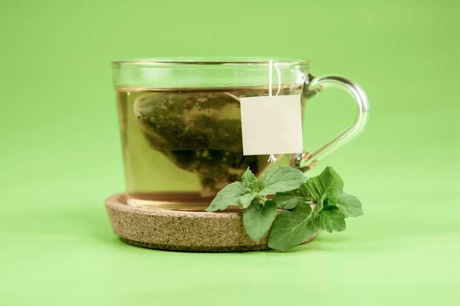 A glass mug of herbal tea with fresh green leaves beside it