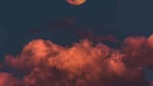 A full moon rising above orange clouds in a deep blue night sky