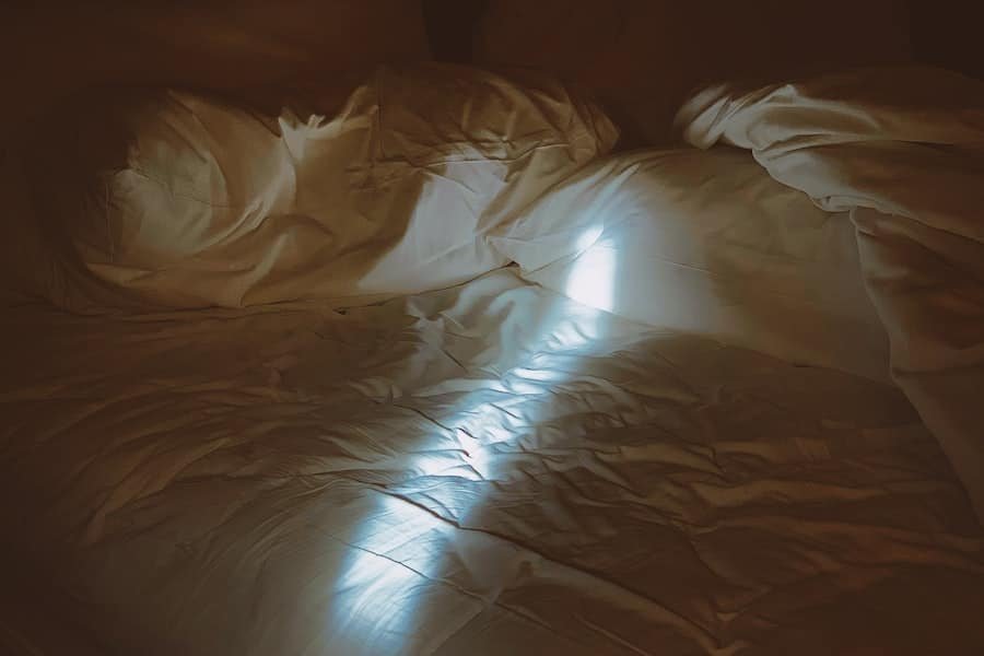 A shaft of daylight across rumpled white bedding