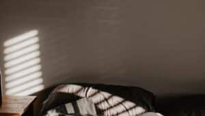 Morning light falling in stripes across a bedroom wall above an unmade bed
