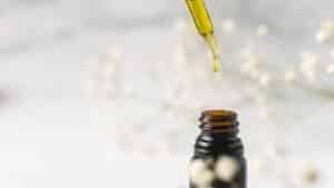 An unlabeled amber dropper bottle with a drop of golden oil above it
