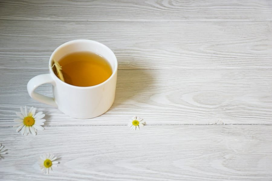 A white cup of herbal tea beside small daisy flowers