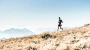 A runner in side view crossing a grassy hillside above misty mountains