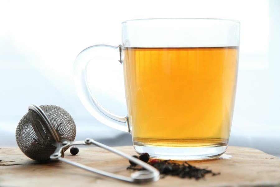 A glass mug of brewed tea beside a metal tea infuser