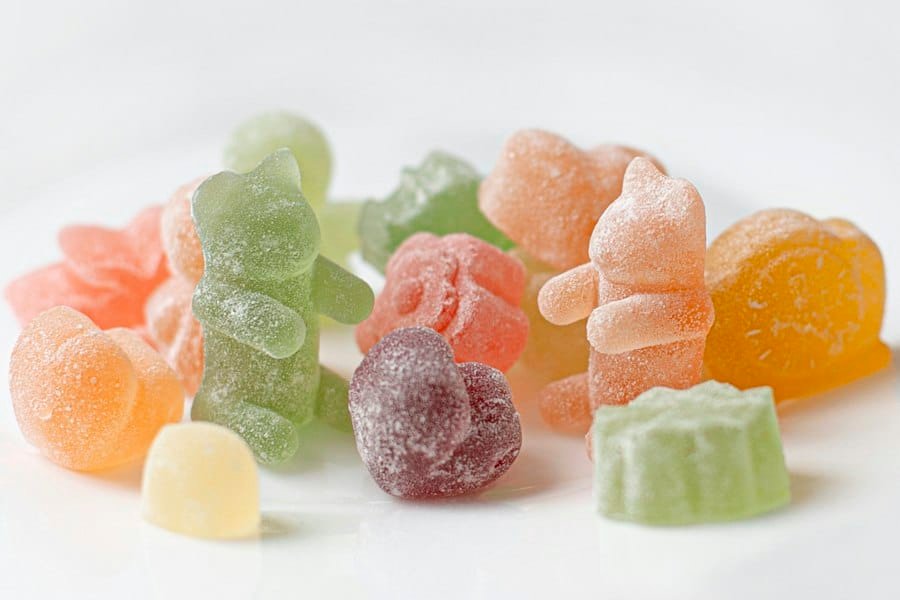 Sugar-coated gummies in assorted shapes and colors on a white surface
