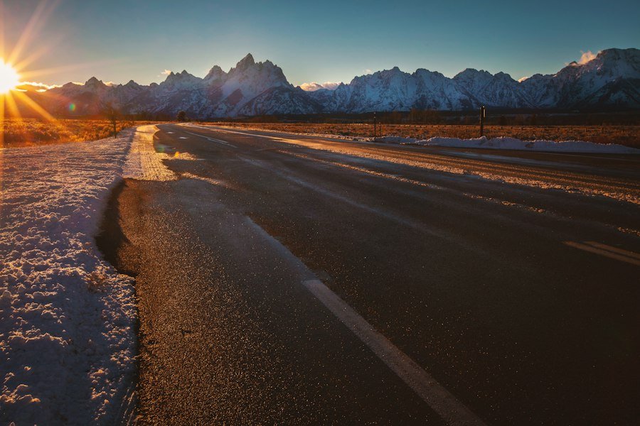 A road running toward snow-capped mountains as the sun rises