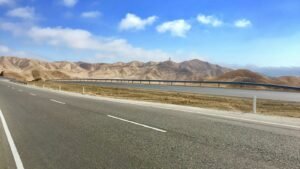 An empty highway curving past dry hills under a blue sky