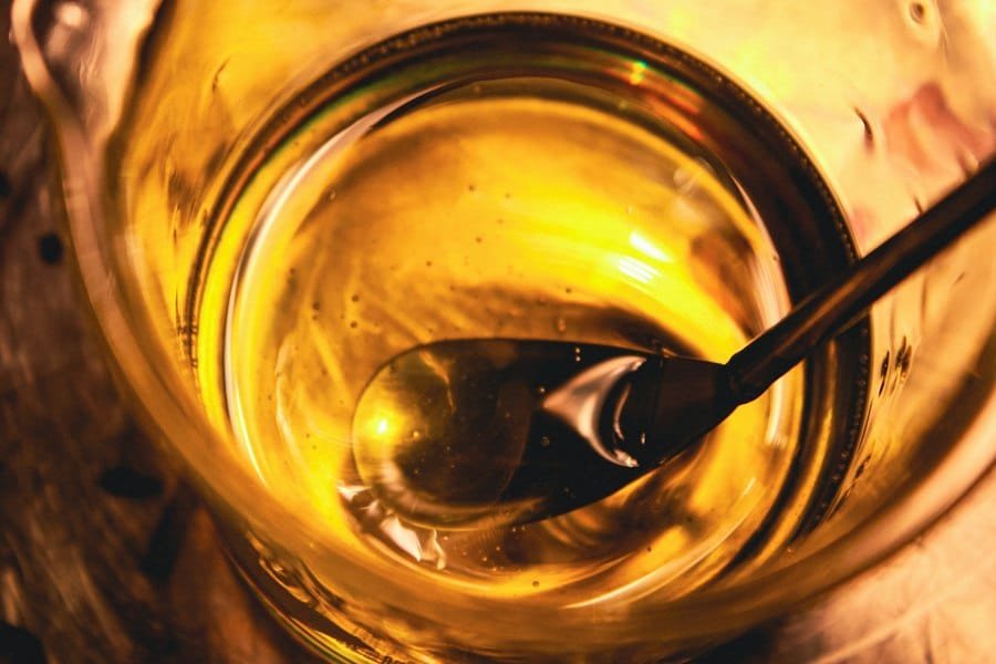 A spoon resting in a glass jar of golden oil