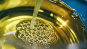 Golden oil being poured into a bowl, forming a cluster of bubbles