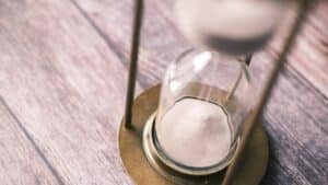 Sand settling in the lower half of an hourglass on a wooden table