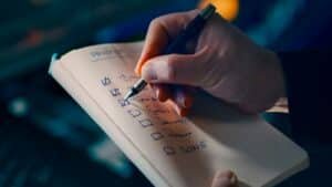 A hand ticking off items on a handwritten checklist in a notebook